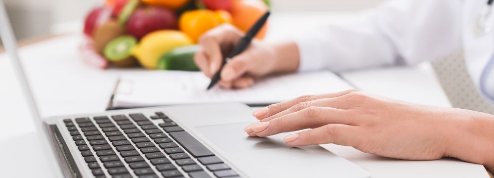 person tracking diet habits on laptop and in notebook with food behind them