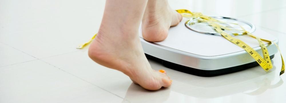 woman stepping on a scale, measuring tape lying on the scale