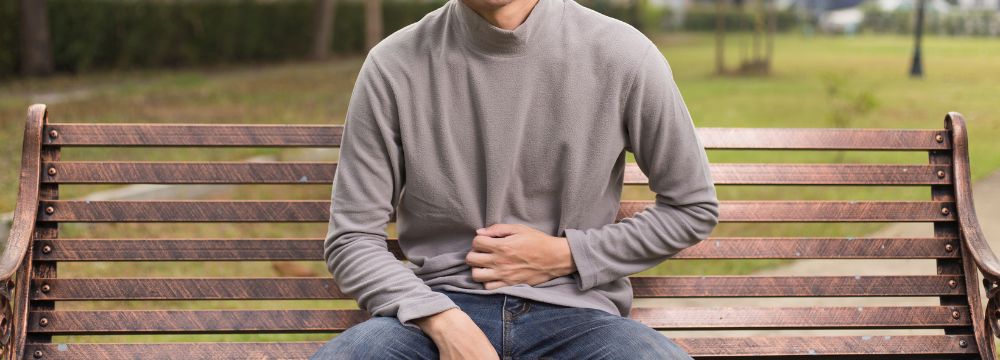 Man sitting on park bench grabbing abdomen from hernia pain due to recurring hernia
