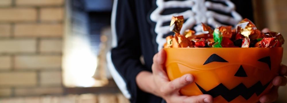 child in halloween costume holding a pumpkin bucket full of halloween candy