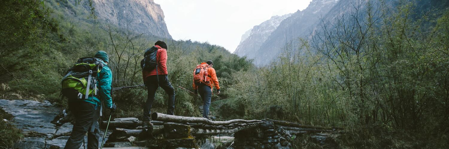 three hikers walking across a bridge while hiking in the mountains 